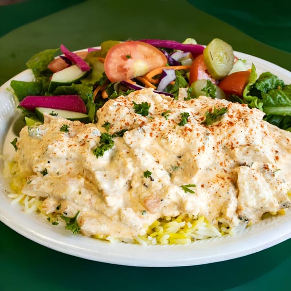 Creamy chicken over rice with a side salad of lettuce, tomatoes, cucumbers, and pickles.