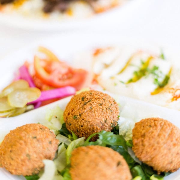 Crispy falafel balls on a bed of lettuce, with hummus, pickles, and tomatoes in the background.