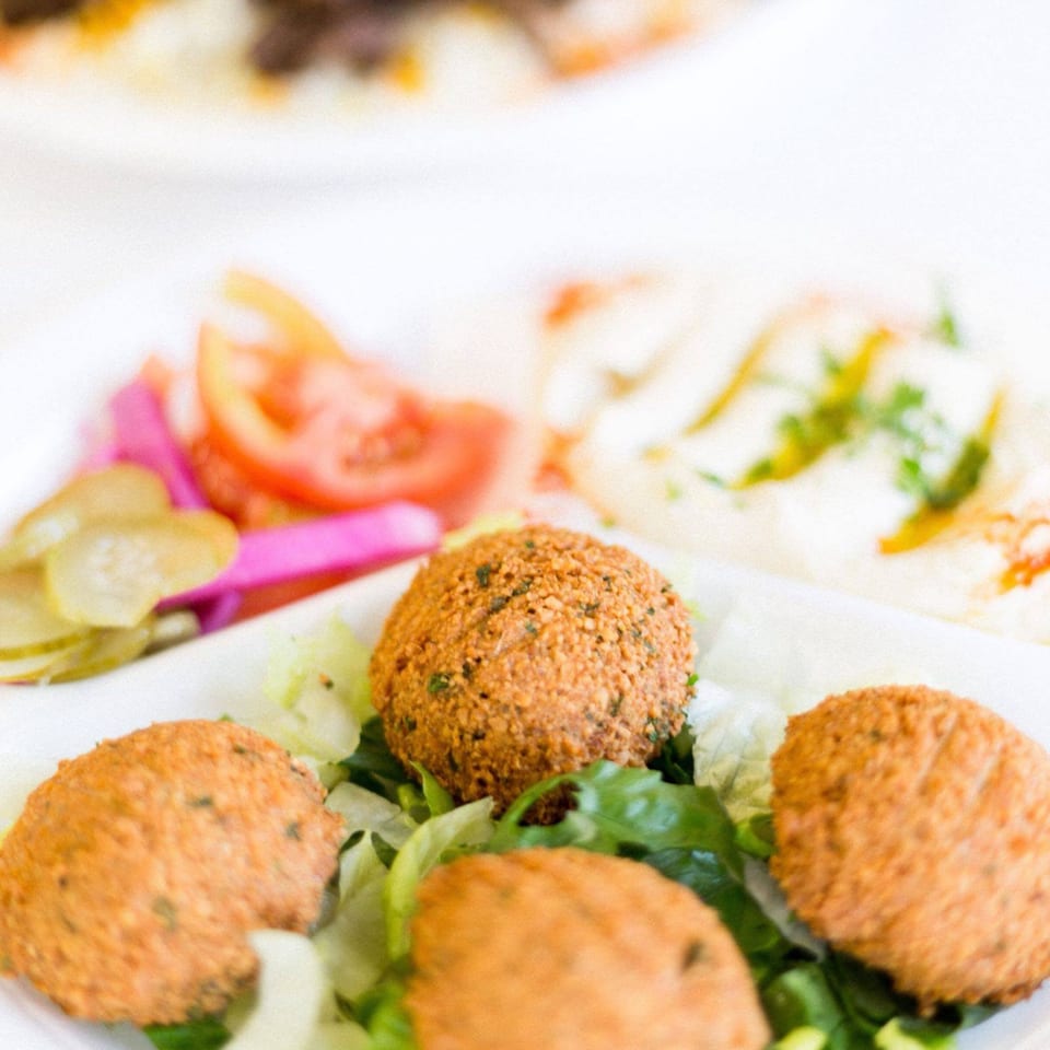 Crispy falafel balls on a bed of lettuce, with hummus, pickles, and tomatoes in the background.