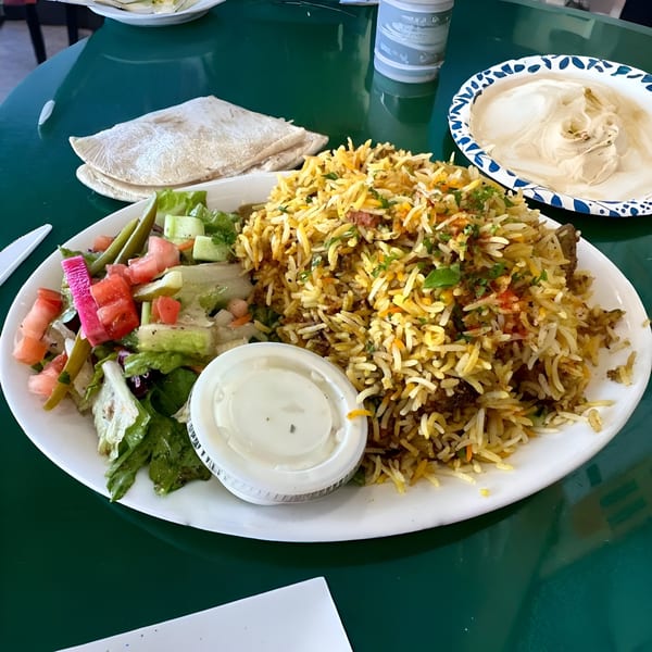 A large plate of Mediterranean biryani rice with salad, pita bread, and hummus on a green table.