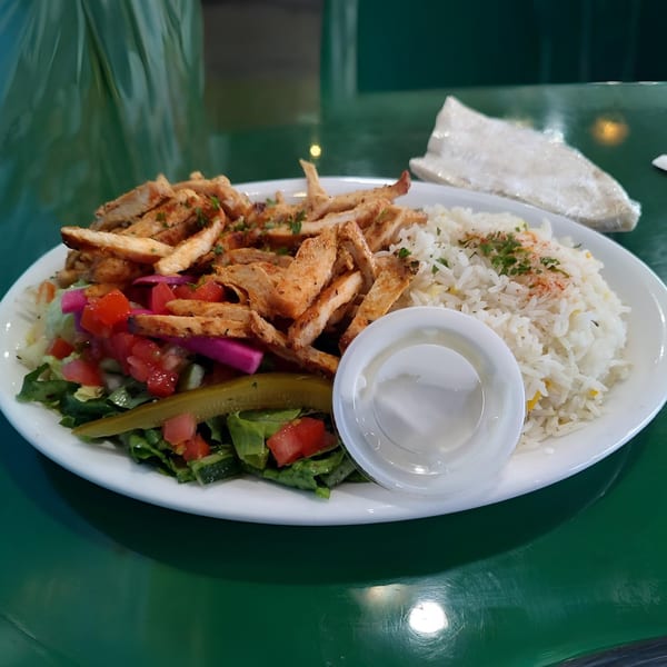 Maira Mediterranean Grill's chicken shawarma plate with rice, salad, pickles, and a side of sauce.