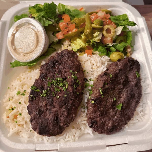 Two grilled Mediterranean beef patties with rice, salad, and a side of sauce in a takeout container.